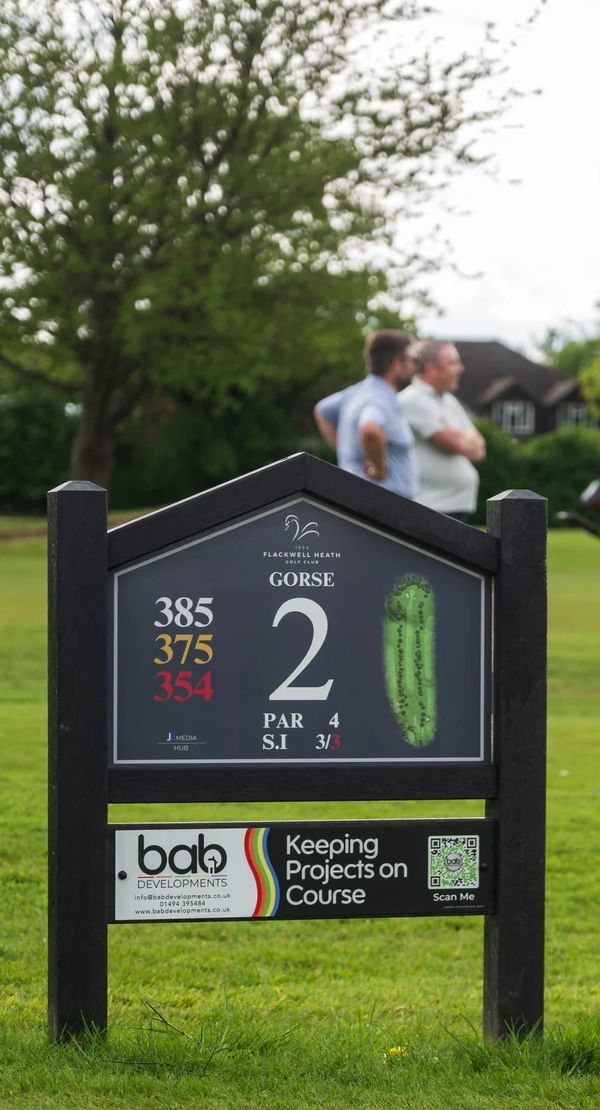 A JB Golf tee sign on the course, with golfers teeing off behind it